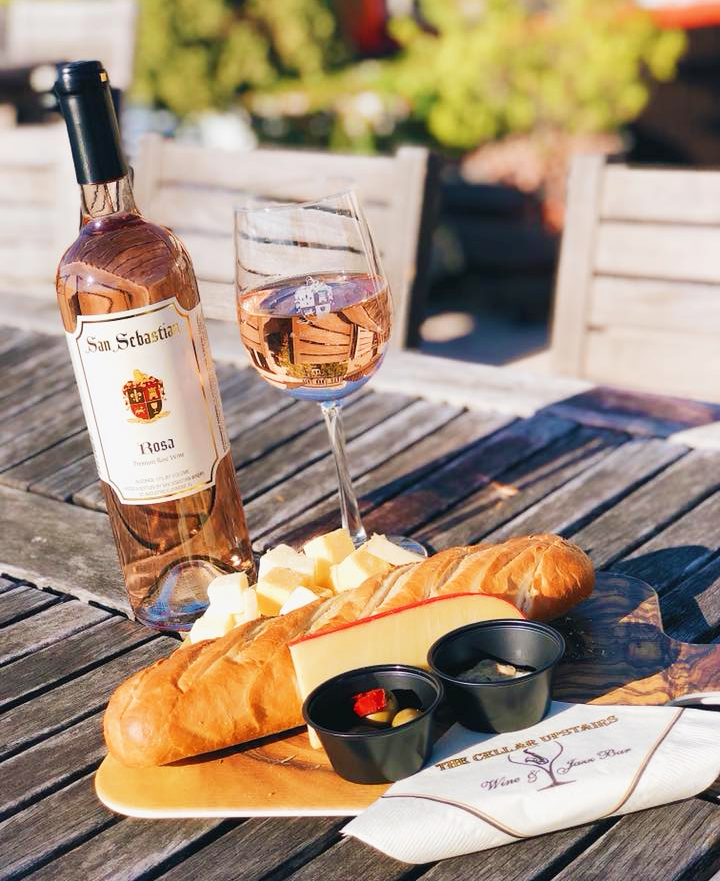 Bottle and glass of The San Sebastian Rosa alongside a platter of cheeses and bread